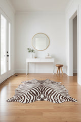 A zebra-print cowhide rug with a natural irregular shape, featuring dark brown and off-white stripes on a white background.