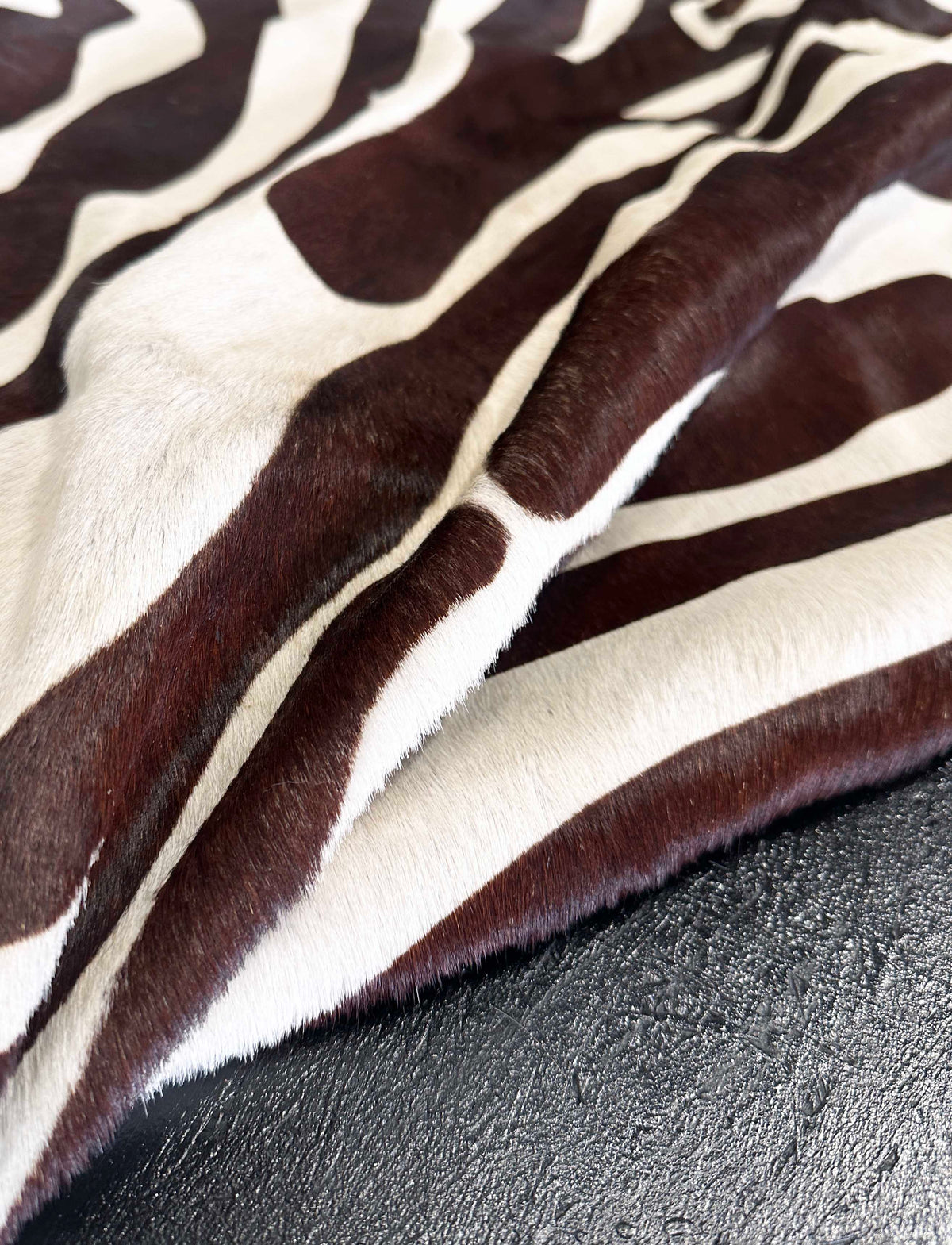 A close-up of a zebra-patterned cowhide rug, showing alternating dark brown and cream stripes, draped over a dark textured surface.