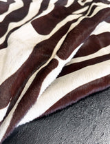 A close-up of a zebra-patterned cowhide rug, showing alternating dark brown and cream stripes, draped over a dark textured surface.