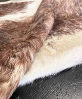 Close-up of a brown and white cowhide fur rug, showing the texture of the hair and the natural color variation, laid over a dark textured surface.