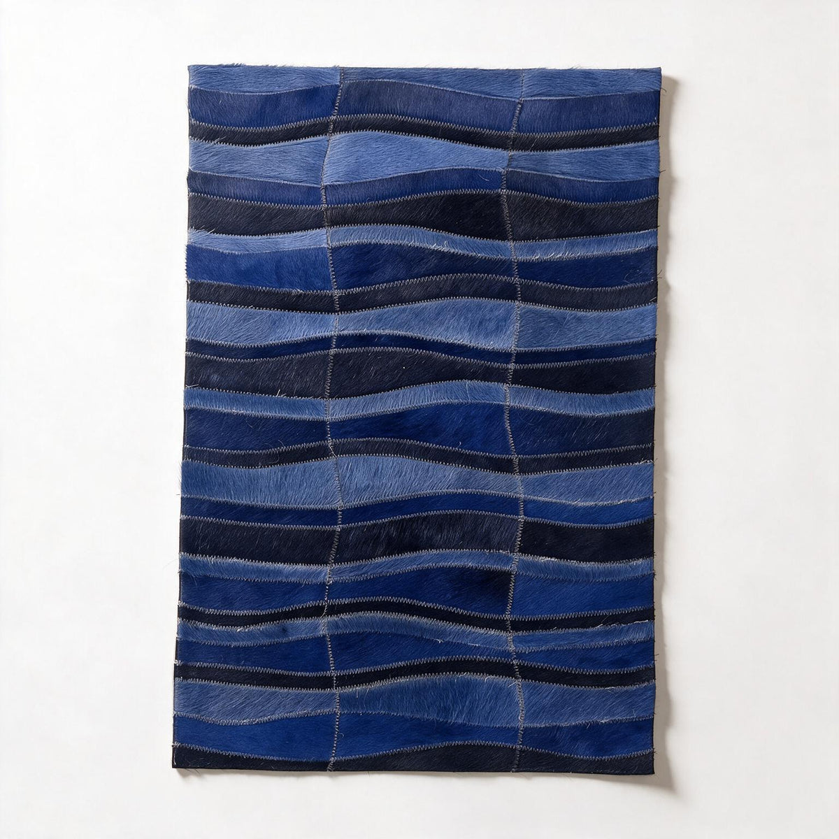 Cavo 16-by-24-inch cowhide rug sample with flowing stitched waves in layered shades of cobalt, denim, and midnight blue.