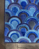 Edge detail of the Ocelli stitched cowhide rug showing nested blue arcs and dark-blue binding