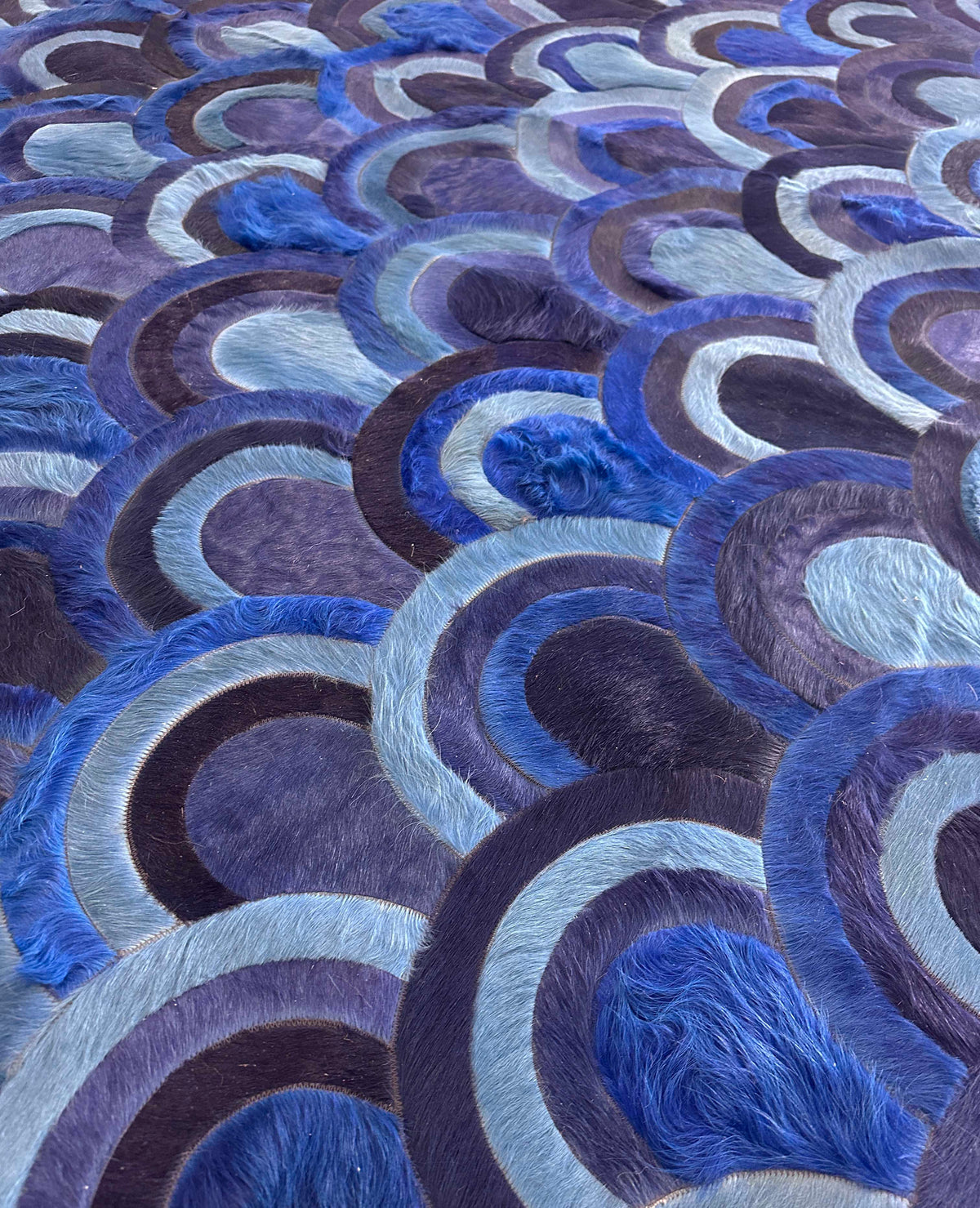 Angled close-up of overlapping peacock-inspired motifs and stitched seams on the Ocelli cowhide rug