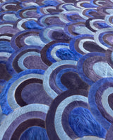 Angled close-up of overlapping peacock-inspired motifs and stitched seams on the Ocelli cowhide rug