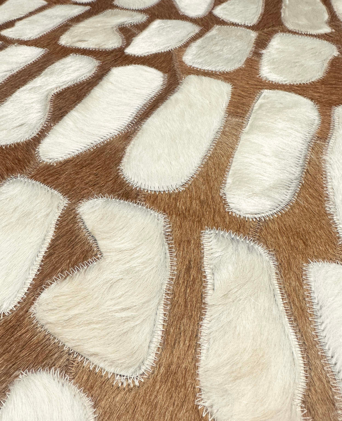 Close-up of Paros ivory cowhide shapes and coordinating zigzag stitching on a warm cognac ground