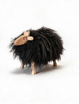 A whimsical sheep figurine with a shaggy black fur body, a light natural wood head and legs, and a small circular cutout detail on its forehead, set against a plain white background.