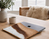 Laptop in a springbok sleeve on a wooden table with a cup and plant in the background