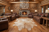Log cabin living room with fireplace, leather furniture, and a cowhide rug.