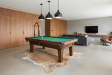 Modern living room with a pool table, leather sofa, and cowhide rug.
