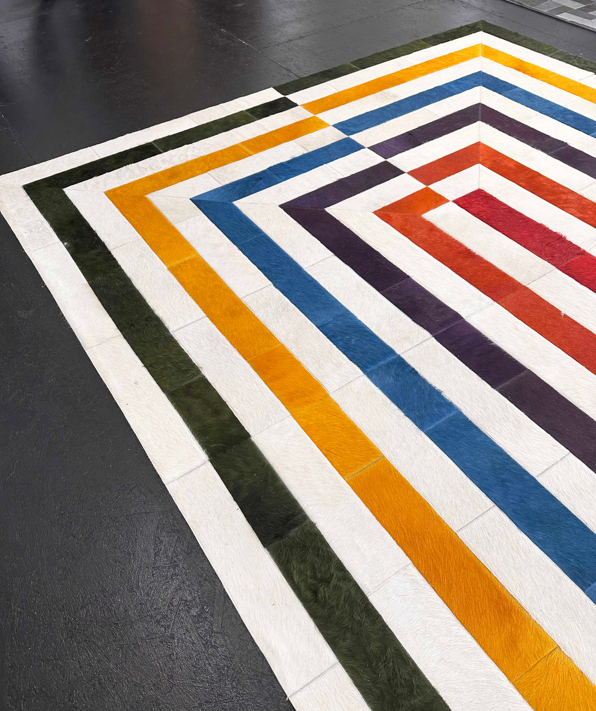 Angled view of a multicolor hair-on cowhide rug showing its nested rectangular pattern and stitched construction