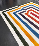 Angled view of a multicolor hair-on cowhide rug showing its nested rectangular pattern and stitched construction