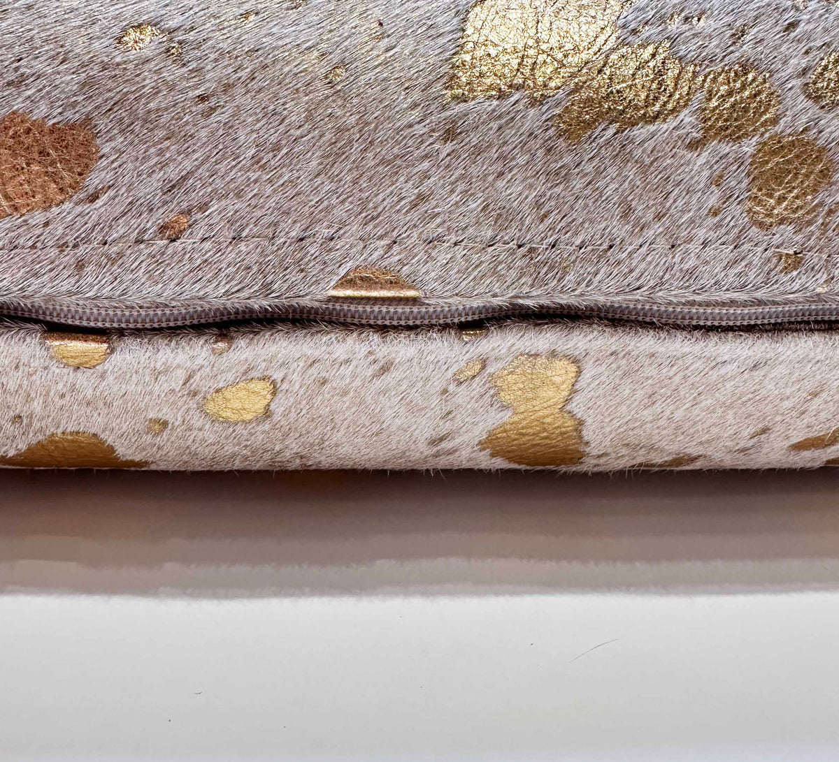 Metallic gold cowhide pillow detail showing hidden zipper and double-sided cowhide
