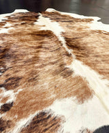 Close-up of a brown and white cowhide rug on a dark floor.