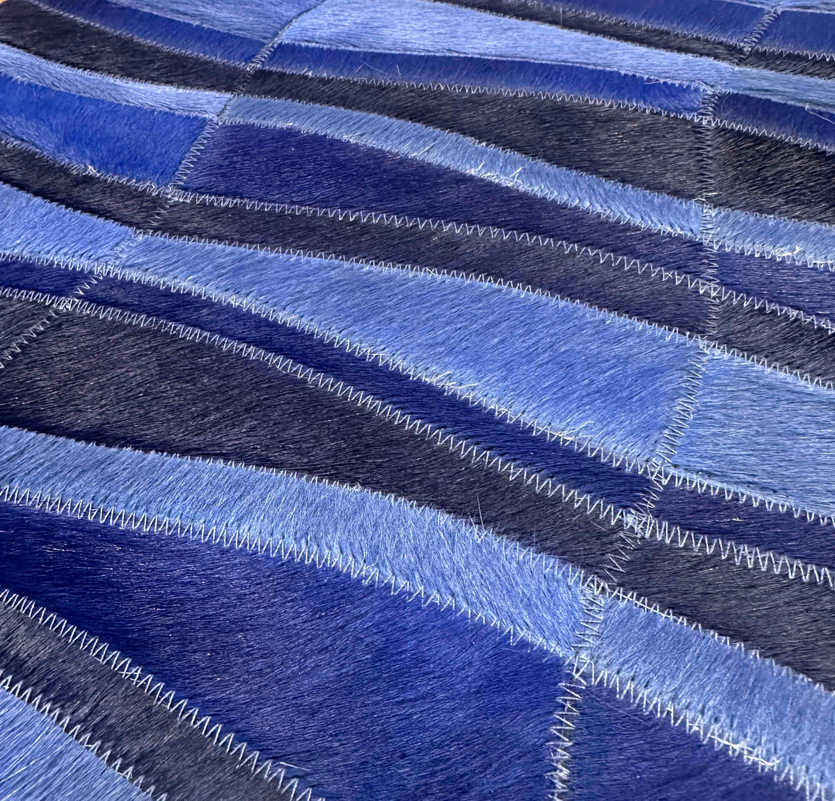 Close-up of the Cavo cowhide rug sample showing undulating blue bands and coordinating stitched seams