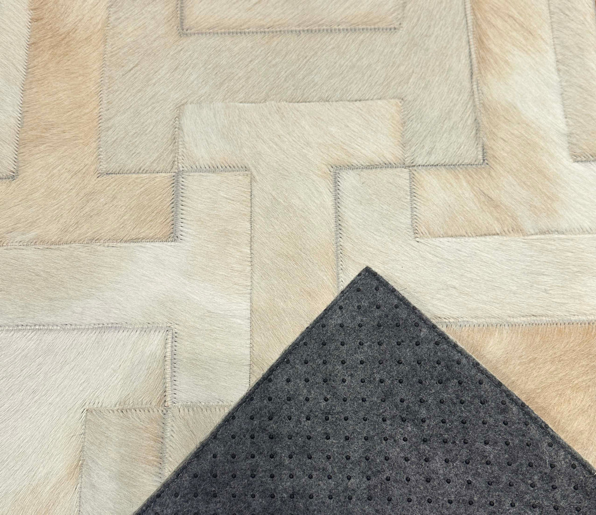 Enchanté stitched cowhide rug sample with a corner turned back to show gray felt backing and black nonslip grip dots
