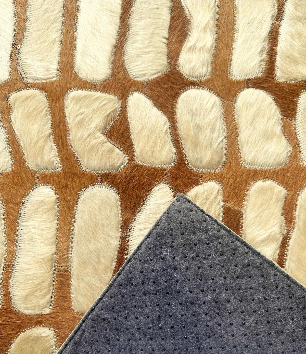 Paros stitched cowhide rug sample with a corner turned back to show gray felt backing and black nonslip grip dots