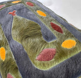 Close-up of hand-stitched cowhide snake motif in olive green and gray-blue