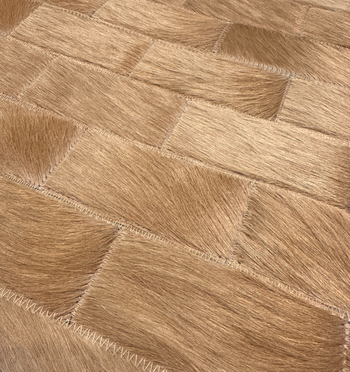 Close-up of Savona’s tonal camel hair-on cowhide rectangles, showing natural hair direction and zigzag stitching.
