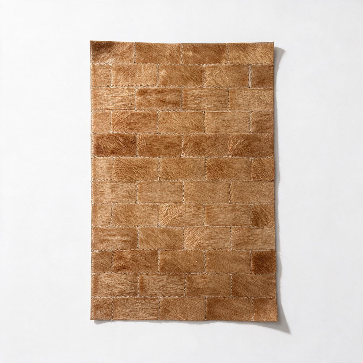 Savona 16-by-24-inch cowhide rug sample with staggered 2-by-4-inch rectangles in caramel and honey-tan tones.
